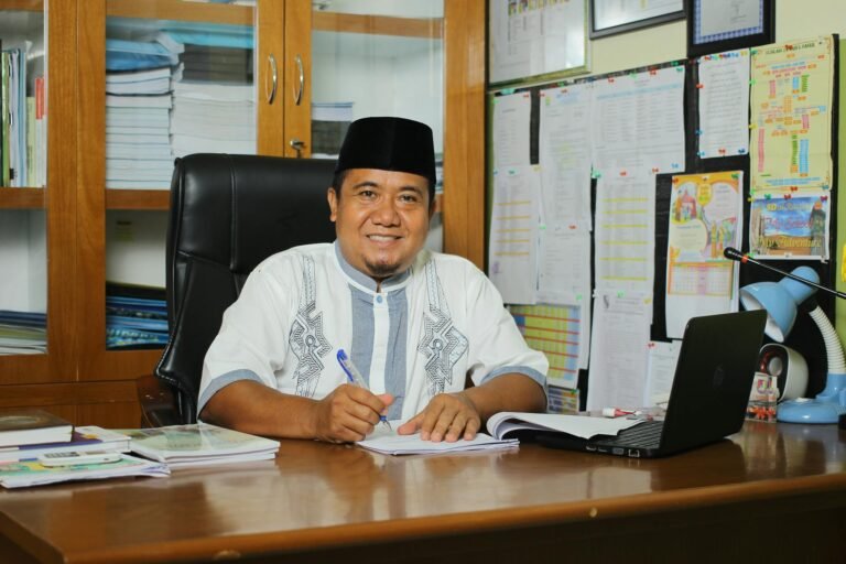 teacher wearing traditional hat sitting by desk